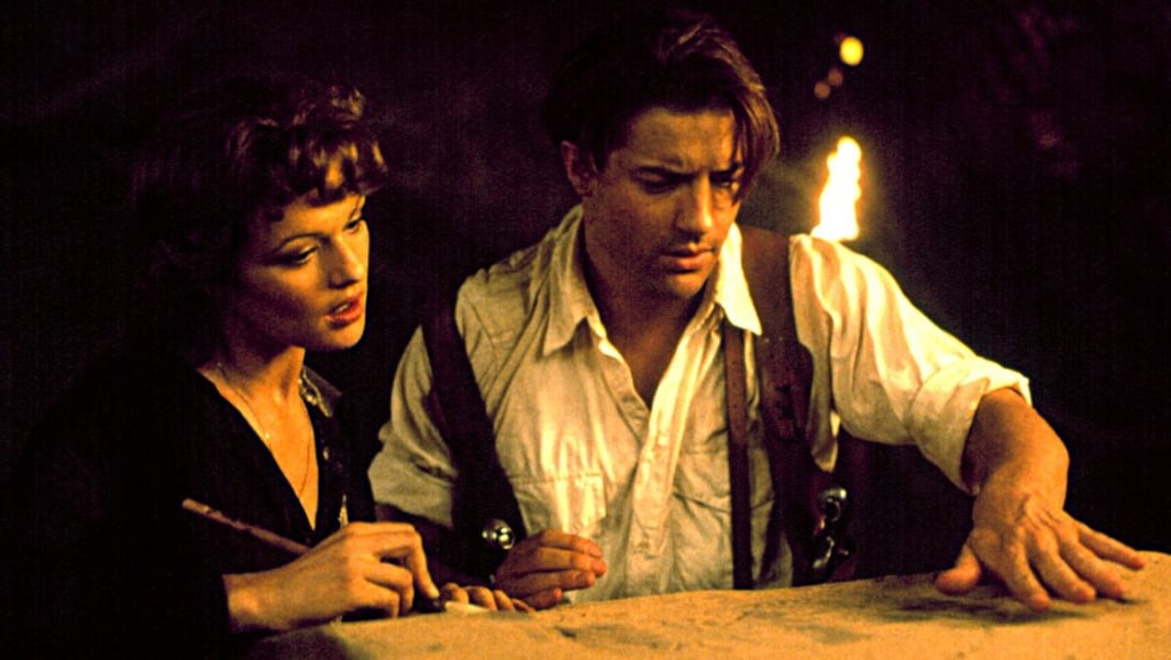 Rachel Weisz and Brendan Fraser study a surface by torchlight in a scene from the 1999 film The Mummy