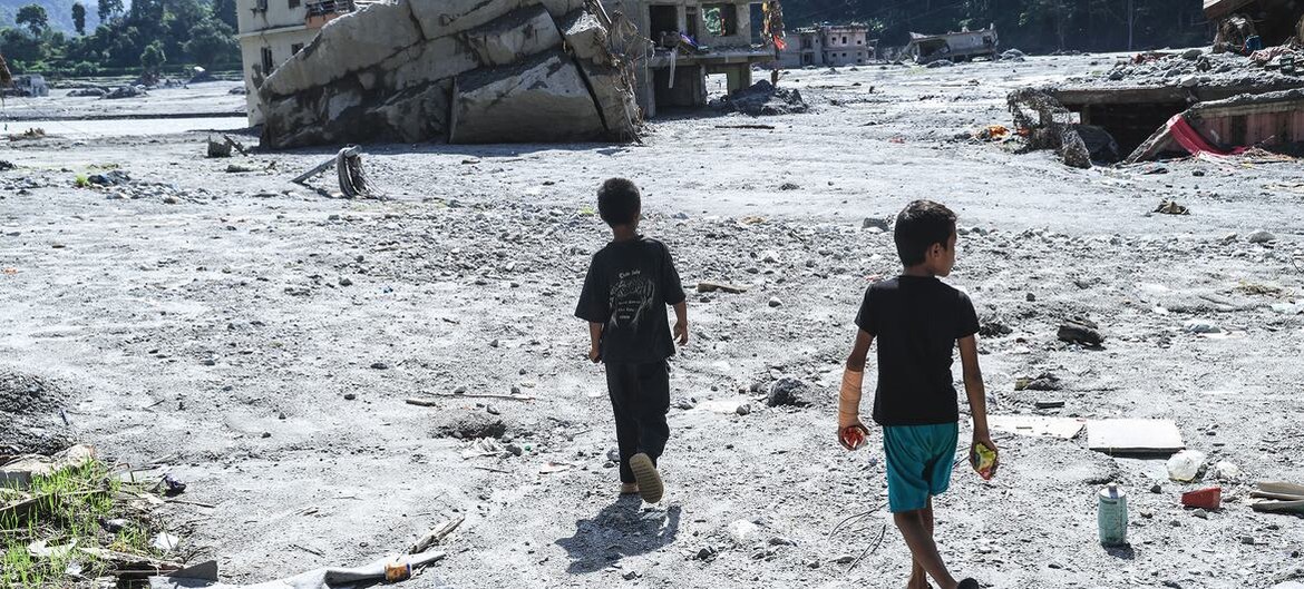Children walk across a flattened, debris-strewn site where their school stood in Nuwakot district, Nepal