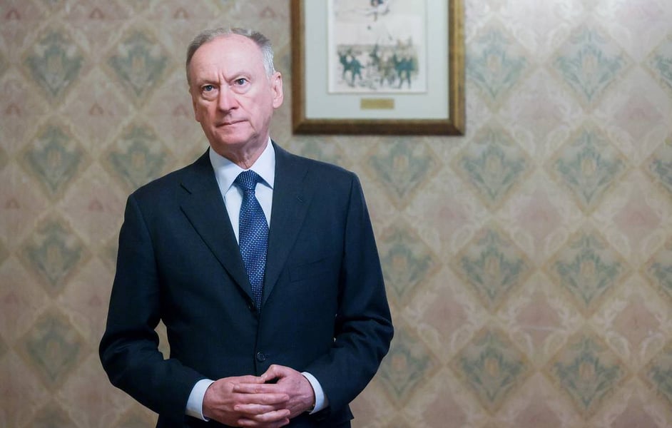 Nikolai Patrushev, Russian presidential aide and chairman of the Maritime Board, standing in a patterned-wallpaper room with his hands clasped