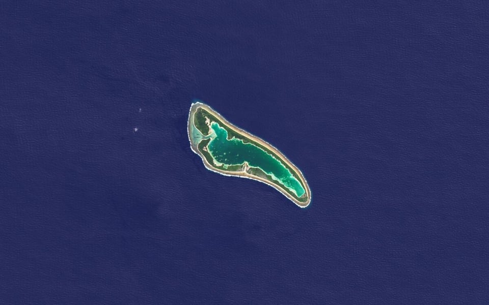 Satellite view of Nikumaroro, a boomerang-shaped coral atoll with a green lagoon, surrounded by dark blue Pacific Ocean