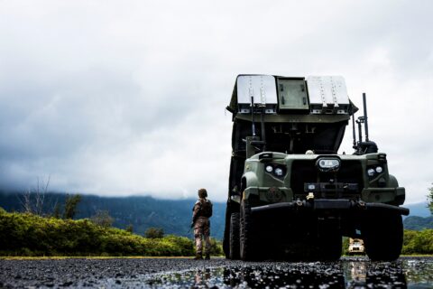 A US Marine stands beside an NMESIS anti-ship missile launcher on a wet road under low cloud at Bellows, Hawaii