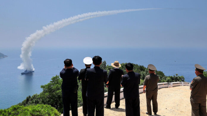 North Korean officials watch a missile climb away from a warship offshore during a July 2026 weapons test