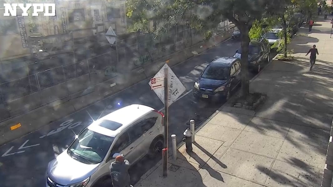 NYPD surveillance camera view of a New York street with a white SUV and parked cars along the curb on the day of an ICE shooting