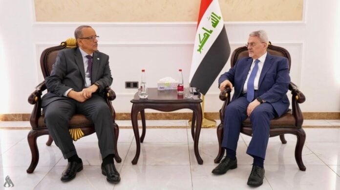 Two officials seated in armchairs beside an Iraqi flag during talks in Baghdad