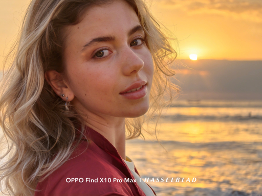 Portrait of a woman in a red jacket beside the ocean at sunset in Oppo Find X10 promotional material.