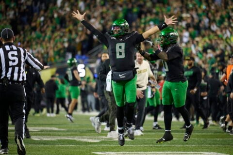 Oregon quarterback Dylan Raiola, wearing No. 8, raises both arms on the field at night as a crowd stands behind him