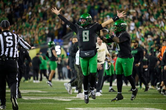 Oregon quarterback Dylan Raiola, wearing No. 8, raises both arms on the field at night as a crowd stands behind him