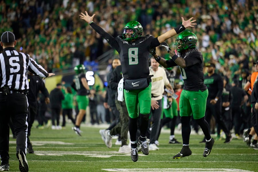 Oregon quarterback Dylan Raiola, wearing No. 8, raises both arms on the field at night as a crowd stands behind him