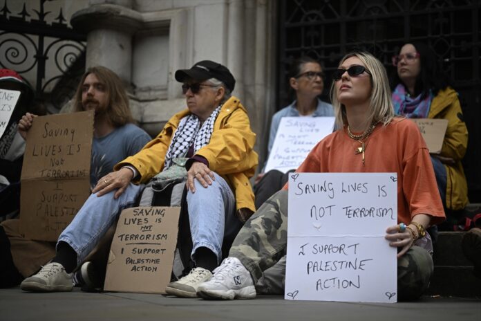 Demonstrators sit holding signs reading Saving lives is not terrorism, I support Palestine Action, outside the Royal Courts of Justice in London