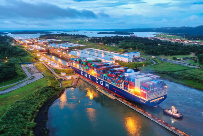 A large container ship with a tugboat beside it moves through a lock of the expanded Panama Canal at dusk