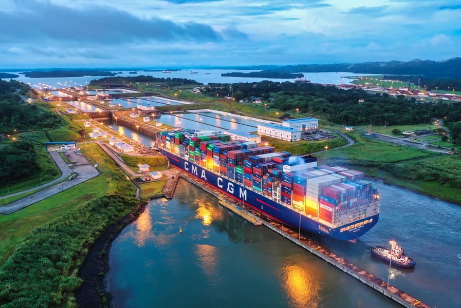 A large container ship with a tugboat beside it moves through a lock of the expanded Panama Canal at dusk