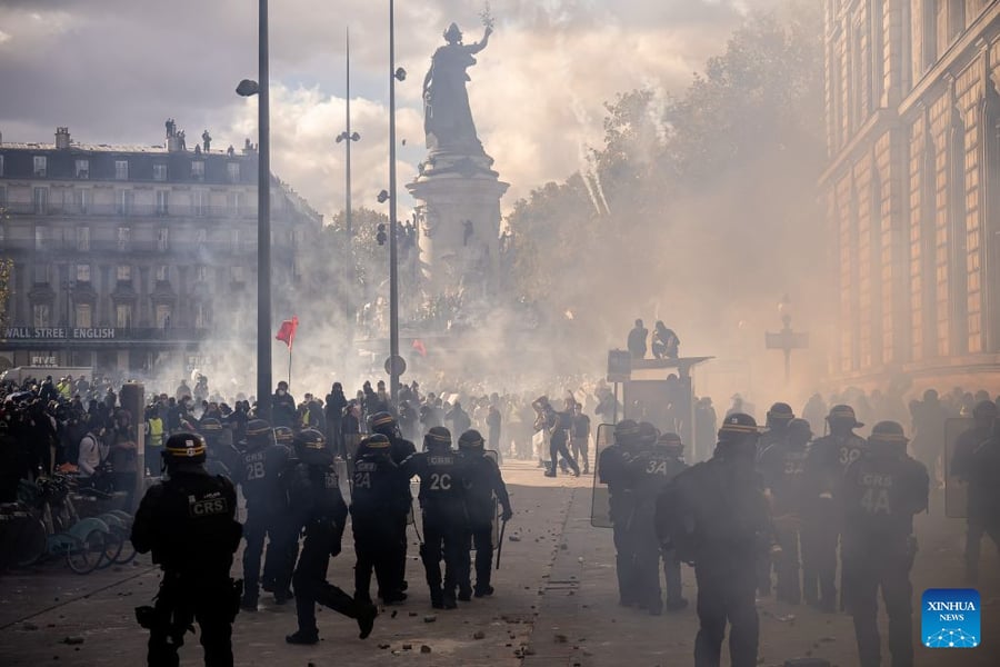 Riot police in helmets and body armour stand in a smoke-filled square in Paris facing a crowd of demonstrators