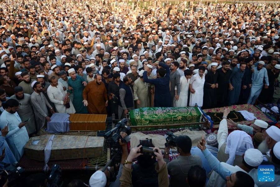 A large crowd of mourners gathers around covered coffins at the funeral of students killed in a school roof collapse in Peshawar