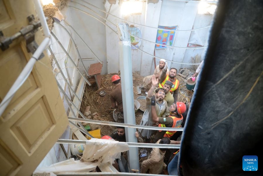 Rescue workers in helmets look up from the floor of a classroom with its roof open, seen from above, at a collapsed school in Peshawar