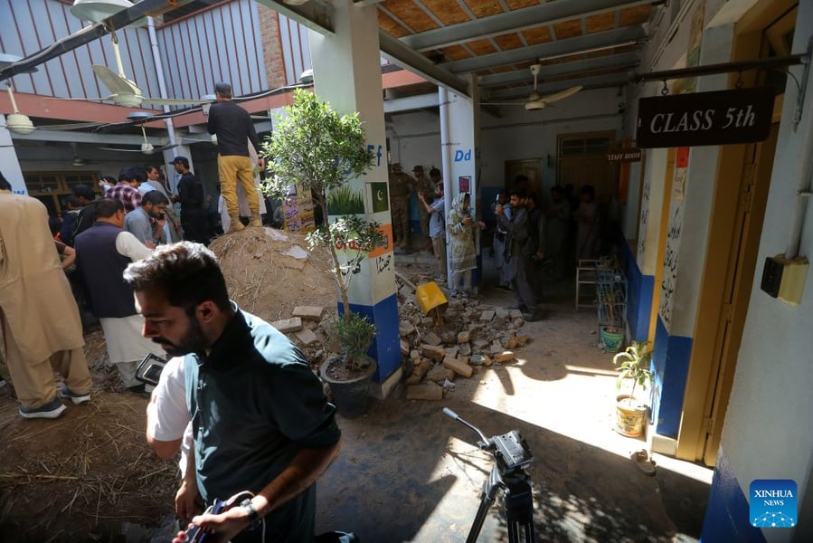 People, journalists and soldiers gather beside bricks and debris in a school courtyard in Peshawar after a roof collapse