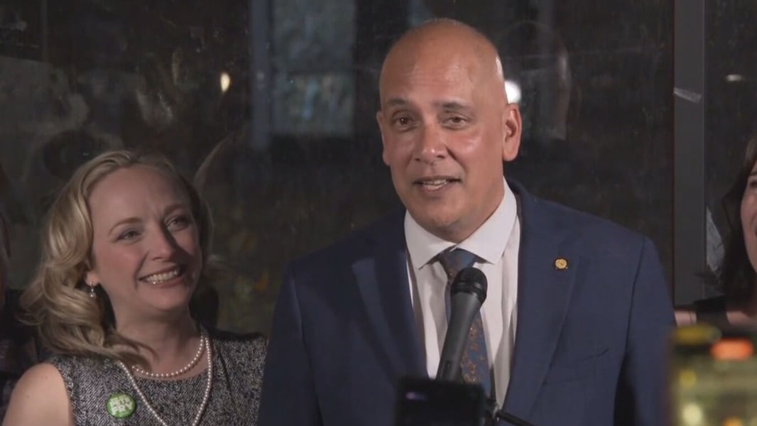 Pete Fry speaking at a microphone on election night, with a supporter wearing a Pete Fry button beside him