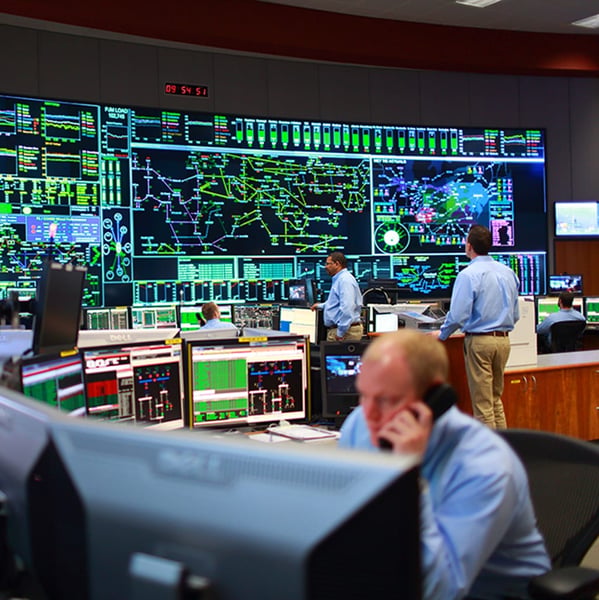 Operators at workstations in front of a wall-sized map of the grid in PJM's control room
