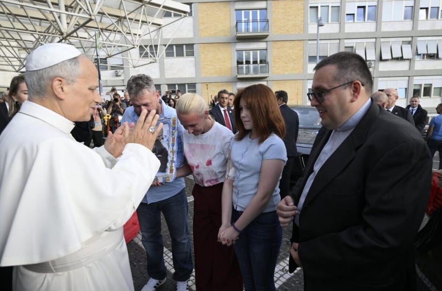 Pope Leo XIV raises his hands toward a teenage girl and two adults, one holding a framed photograph, outside Gemelli Hospital