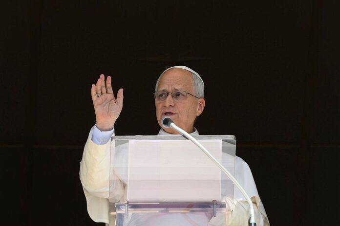 Pope Leo XIV raises his right hand in blessing at a clear lectern during the Sunday Angelus