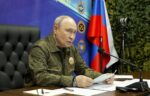 Vladimir Putin in military-style jacket speaks at a table with a microphone and Russian flag behind him at a Joint Force command post