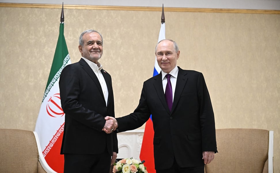 Vladimir Putin and Iranian President Masoud Pezeshkian shake hands in front of Russian and Iranian flags in Turkmenbashi