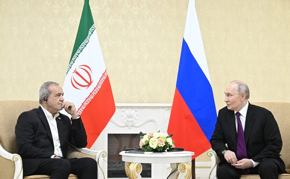 Iranian President Masoud Pezeshkian and Vladimir Putin seated beside Iranian and Russian flags during talks in Turkmenbashi