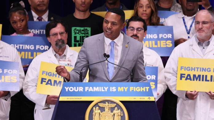 Rep. Ritchie Torres speaking at a podium in front of a crowd holding signs