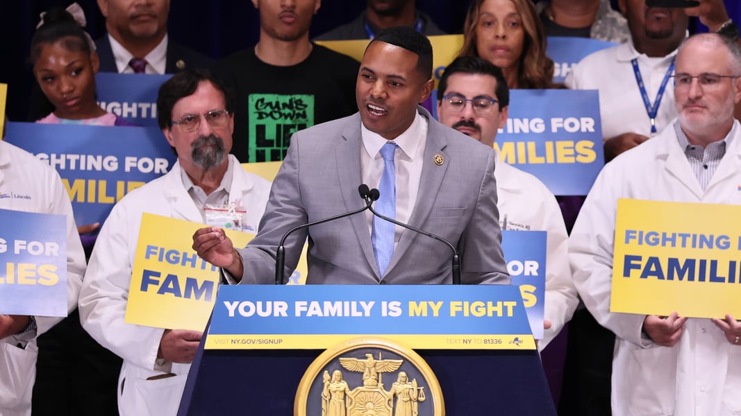 Rep. Ritchie Torres speaking at a podium in front of a crowd holding signs