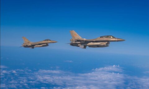 Two Romanian Air Force F-16 fighter jets flying side by side above clouds