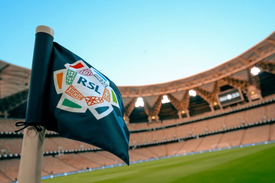 A Roshn Saudi League corner flag in the foreground of a floodlit stadium with an empty pitch