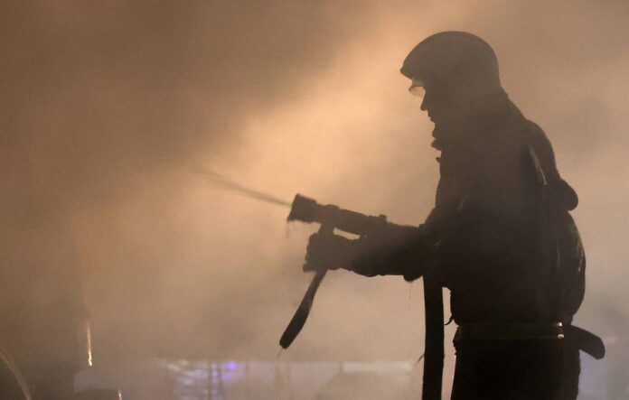 Silhouette of a firefighter spraying water through smoke at a fire scene