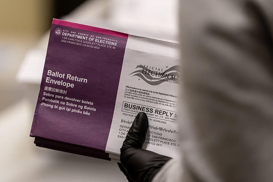 A gloved hand holds a purple and white San Francisco Department of Elections ballot return envelope