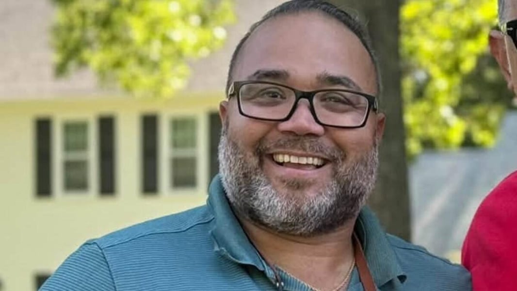 Shawn Oliver, a bearded man in glasses and a teal polo shirt, smiling outdoors in a campaign photo