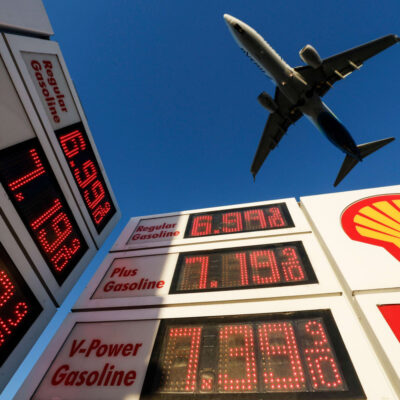 A jet approaches San Diego airport above a Shell station sign showing gasoline prices of about $7 to $8 a gallon