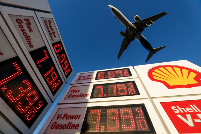A jet approaches San Diego airport above a Shell station sign showing gasoline prices of about $7 to $8 a gallon