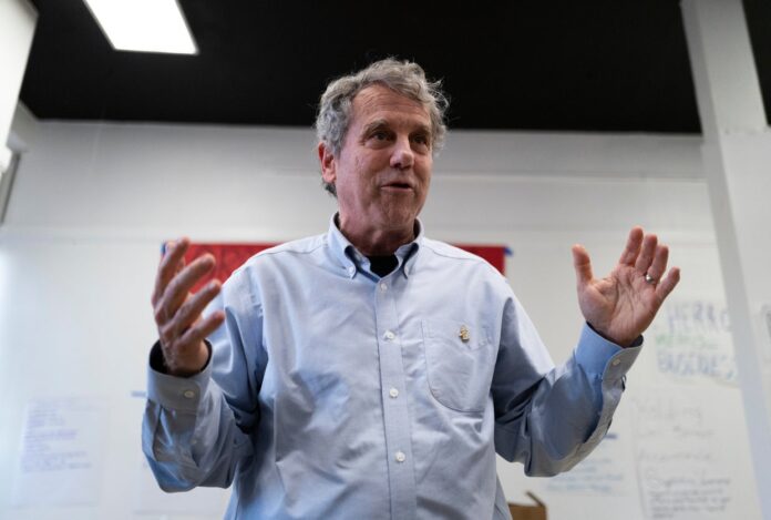 Sherrod Brown speaking with both hands raised at a campaign office