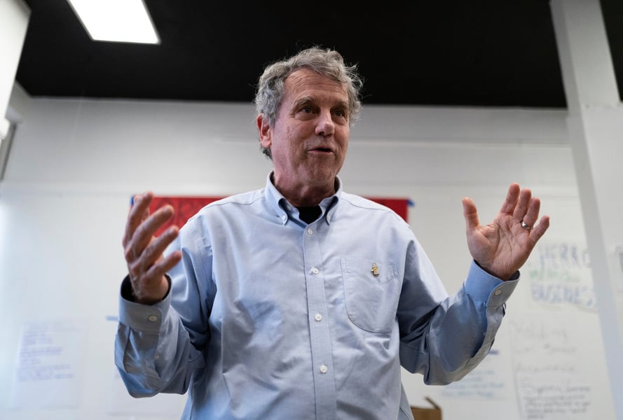 Sherrod Brown speaking with both hands raised at a campaign office