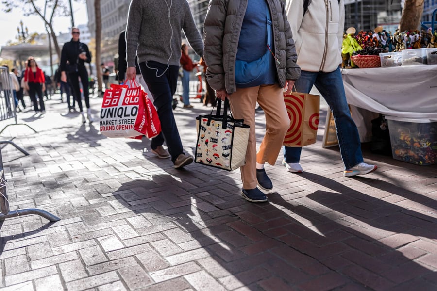 Shoppers carrying retail bags walk along a brick-paved city sidewalk