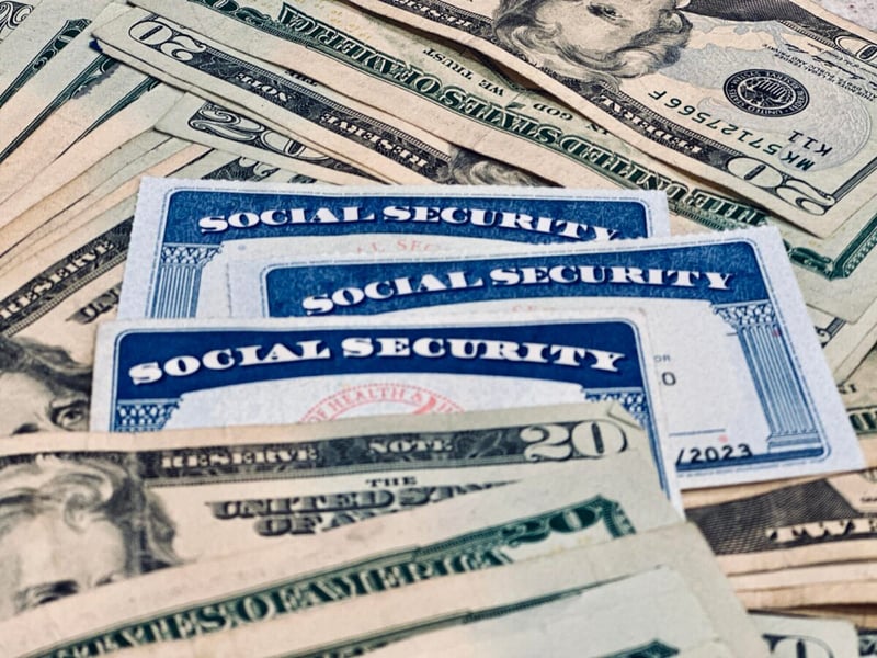 Three Social Security cards fanned out on a pile of 20-dollar bills