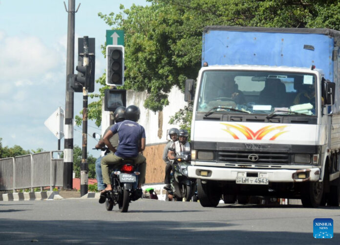 Motorcyclists and a truck pass a traffic light that is not working at a junction in Colombo, Sri Lanka