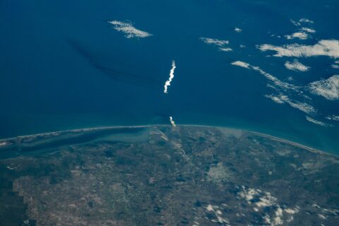 Starship's white launch plume rising over the Gulf of Mexico off the Texas coast, photographed from the International Space Station