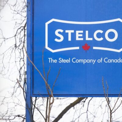 Blue Stelco sign reading The Steel Company of Canada, with bare branches in front of it