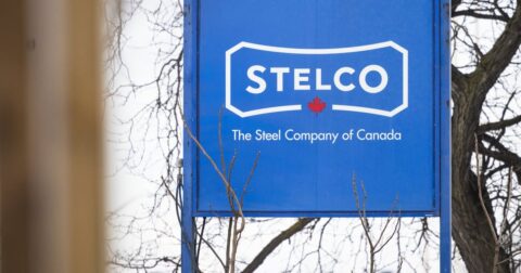 Blue Stelco sign reading The Steel Company of Canada, with bare branches in front of it