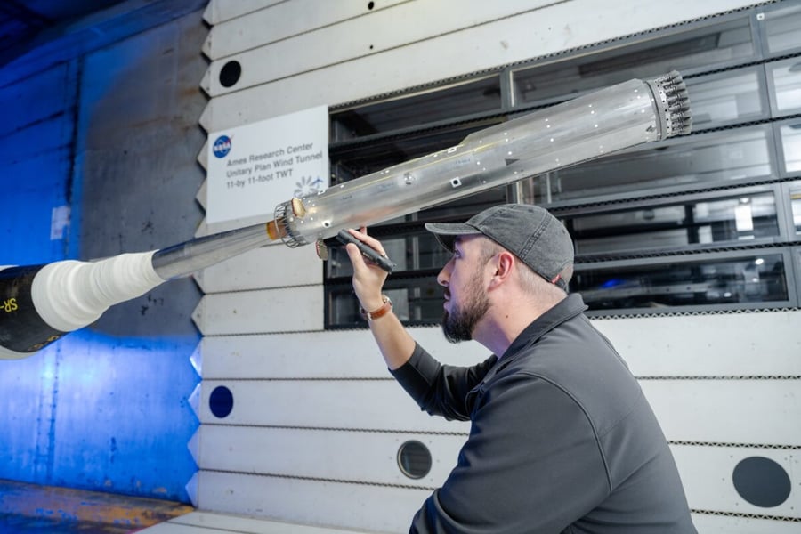 A man in a cap inspects a metal scale model of a rocket booster with engine nozzles mounted in a NASA Ames Research Center wind tunnel