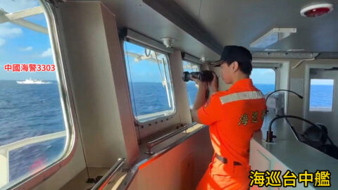 Taiwan Coast Guard officer in an orange uniform photographs a distant China Coast Guard vessel labelled 3303 from the bridge of the patrol ship Taichung
