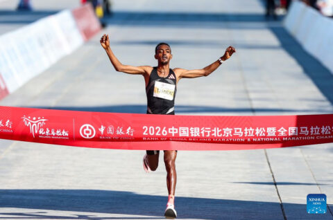 Tamirat Tola of Ethiopia, arms spread, breaks the finish-line tape at the 2026 Beijing Marathon