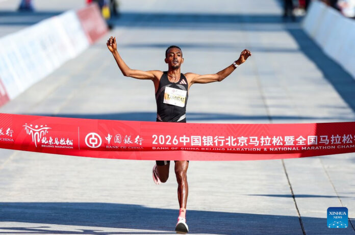 Tamirat Tola of Ethiopia, arms spread, breaks the finish-line tape at the 2026 Beijing Marathon