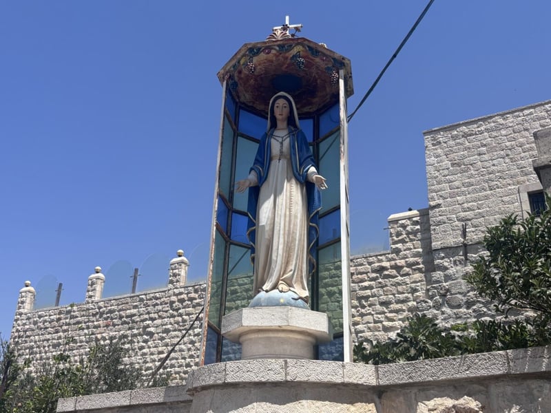 Statue of the Virgin Mary in a glass shrine beside a stone wall in the West Bank town of Taybeh