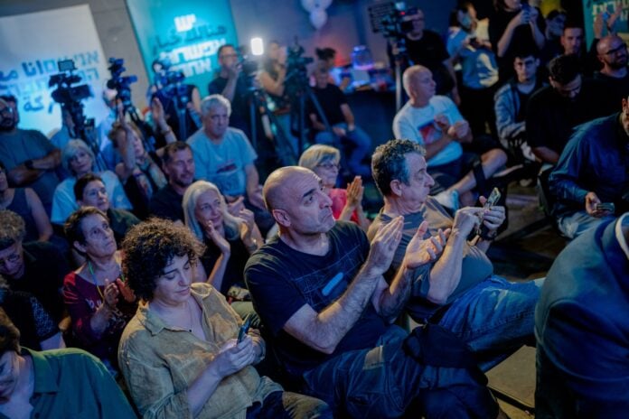 Attendees applaud and film on phones at an election campaign meeting in Tel Aviv ahead of Israel's October 27 vote
