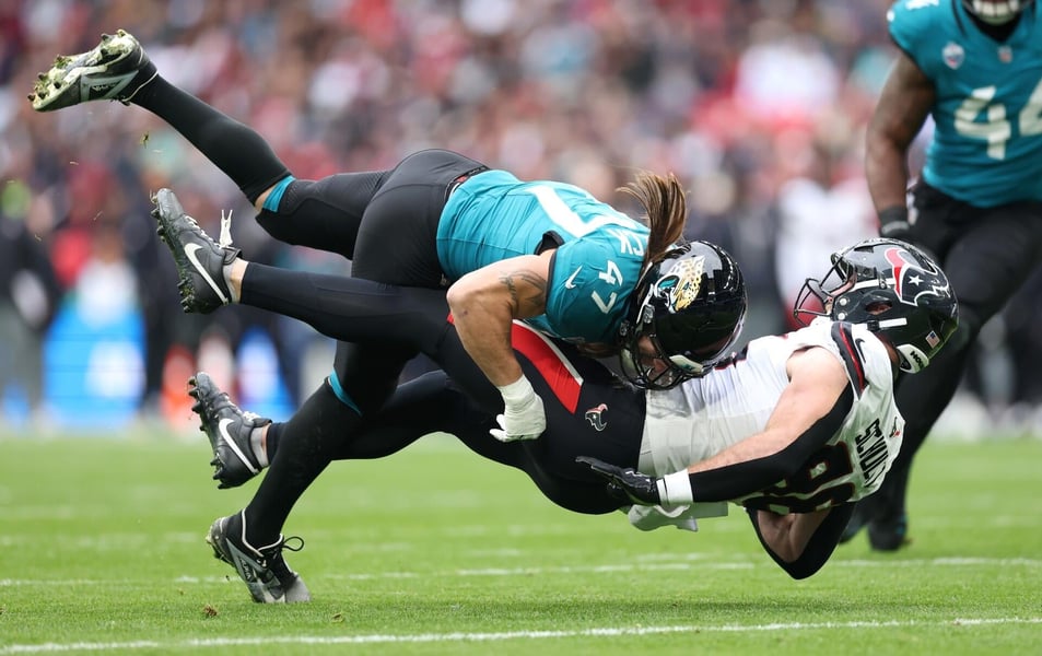 A Jacksonville Jaguars defender in a teal jersey and a Houston Texans player in white collide in mid-air during the game in London